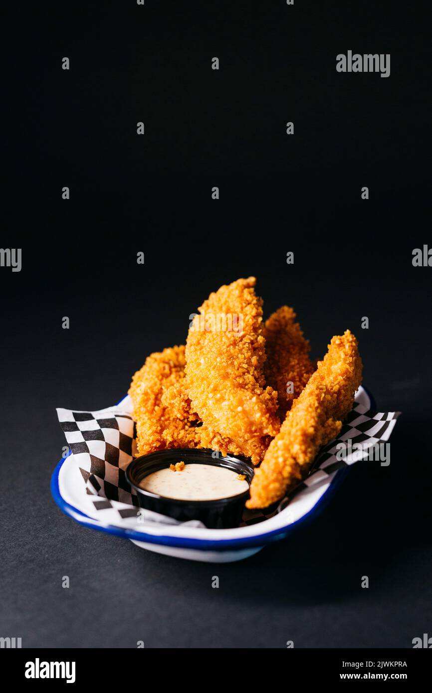 Hähnchenfinger mit Mayonnaise-Sauce auf einem Teller auf schwarzem Hintergrund Stockfoto