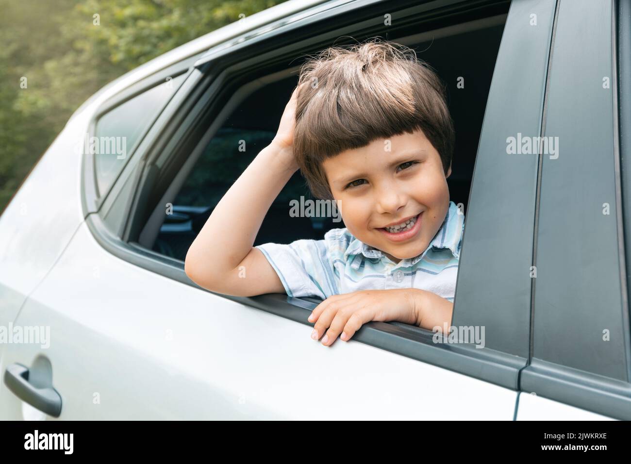Fröhliches kaukasisches kleines Kind fährt mit dem Auto in den Urlaub und schaut aus dem Fenster, genießt Reise und Wochenende, draußen Stockfoto
