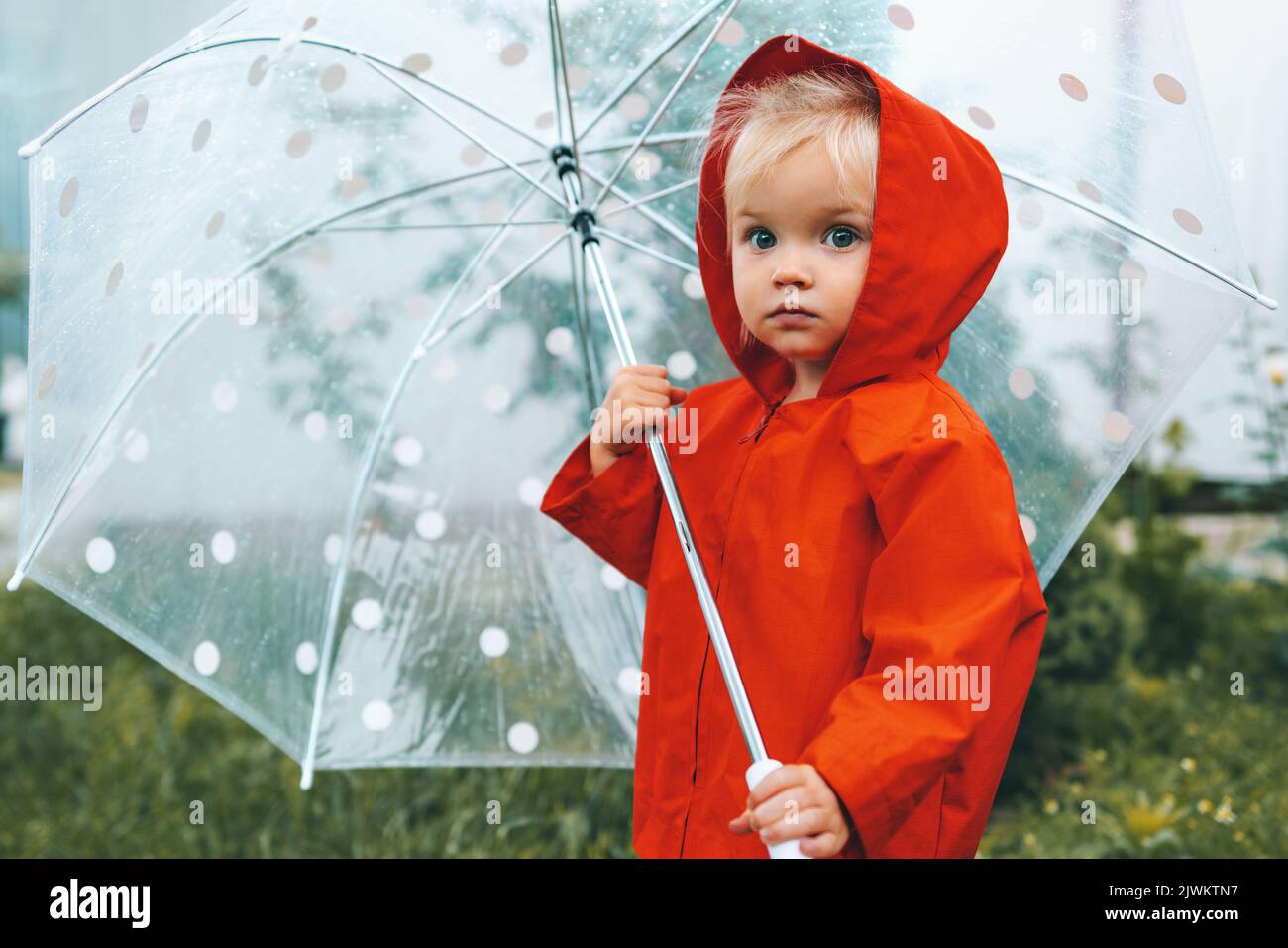 Herbstsaison Kind mit Regenschirm zu Fuß im Freien trägt roten Regenmantel regnerisches Wetter 2 Jahre alt Kind Stockfoto