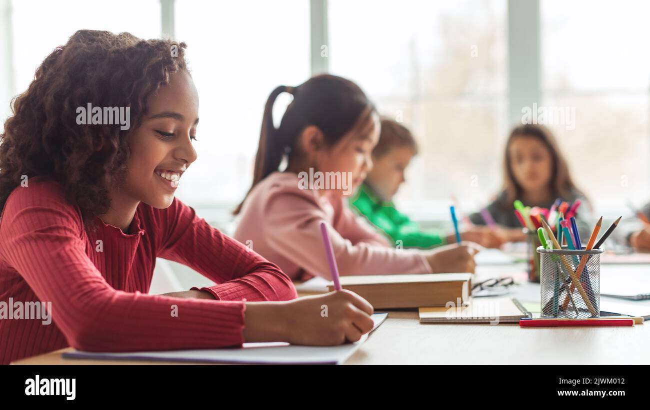 Schwarz Schulmädchen Schreiben Lernen Mit Multikulturellen Klassenkameraden Im Klassenzimmer, Panorama Stockfoto