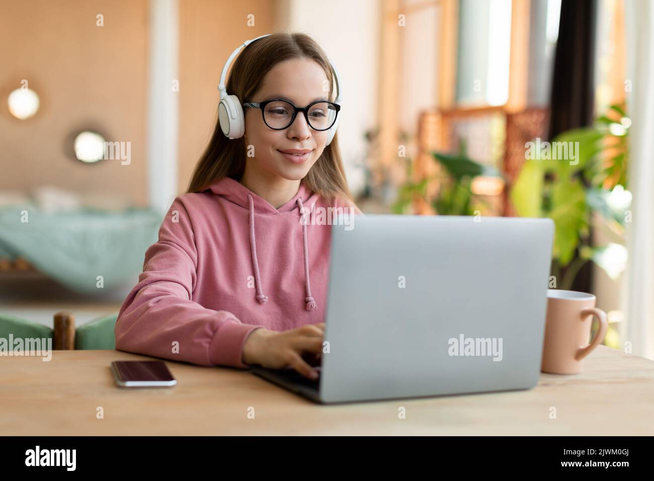 Hübsches Teenager-Mädchen in schnurlosem Headset mit Laptop, interessierte glückliche Schüler tippen auf der Tastatur Blick auf pc-Bildschirm Stockfoto