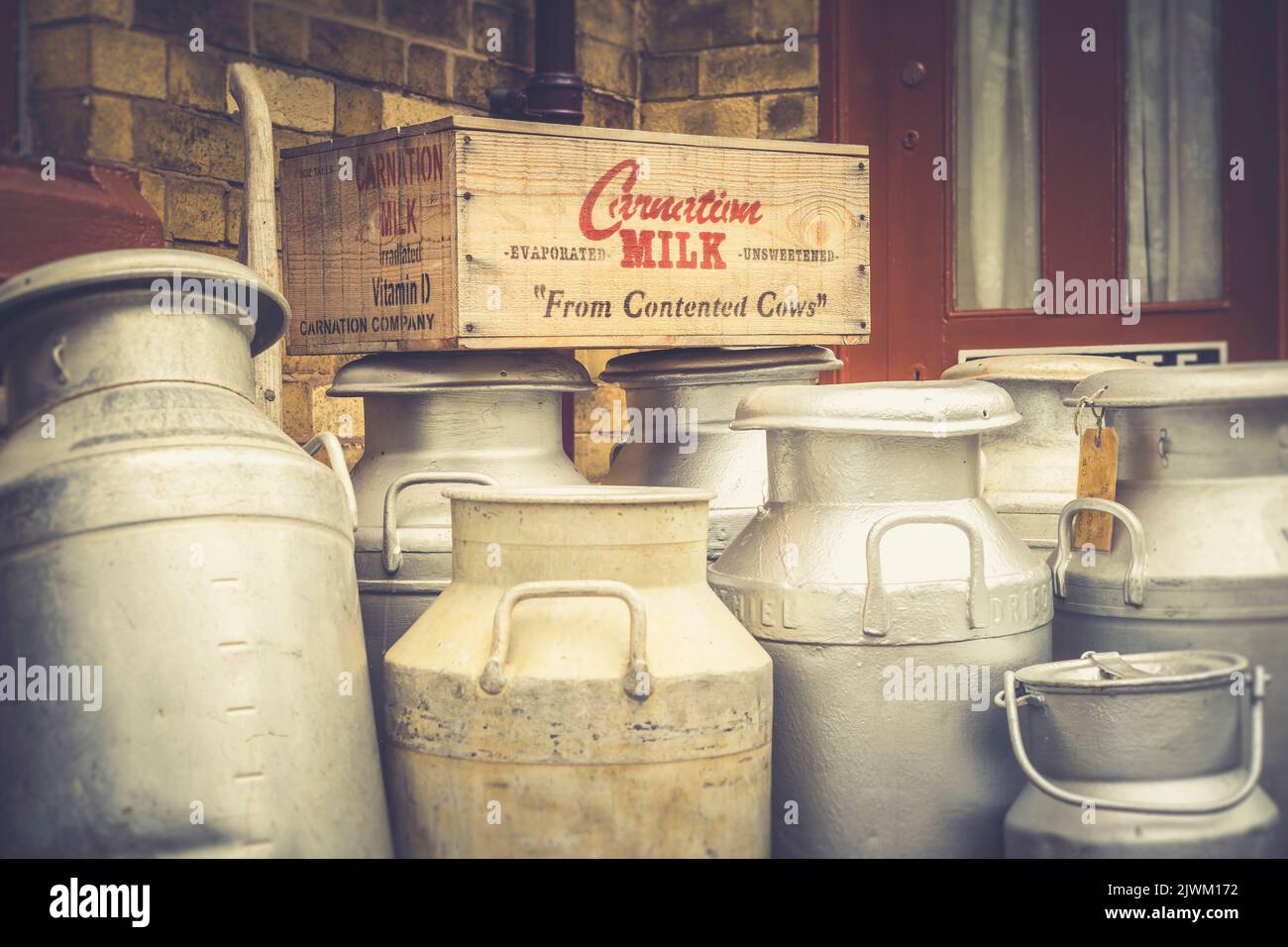 Vintage Milk Churns auf dem Bahnsteig eines historischen britischen Bahnhofs zusammen mit einer alten Holzkiste Carnation Verdunsteter Milch. Stockfoto