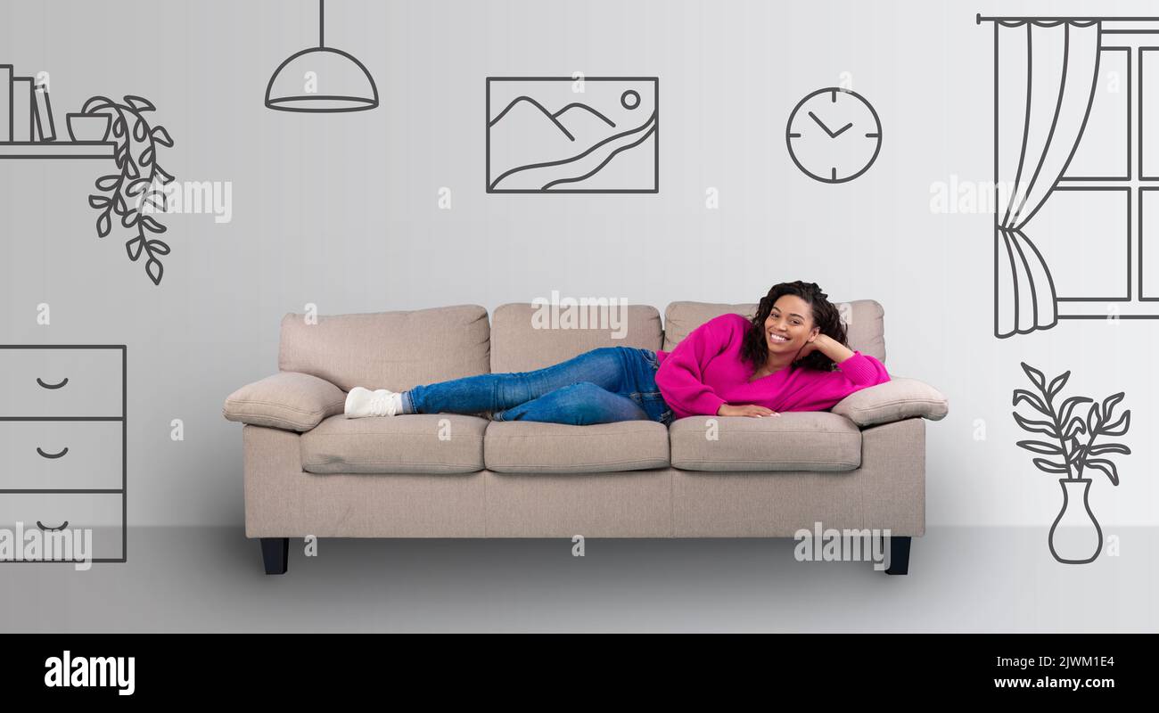 Schöne glückliche junge schwarze Frau, die auf dem Sofa liegt und lächelt Stockfoto