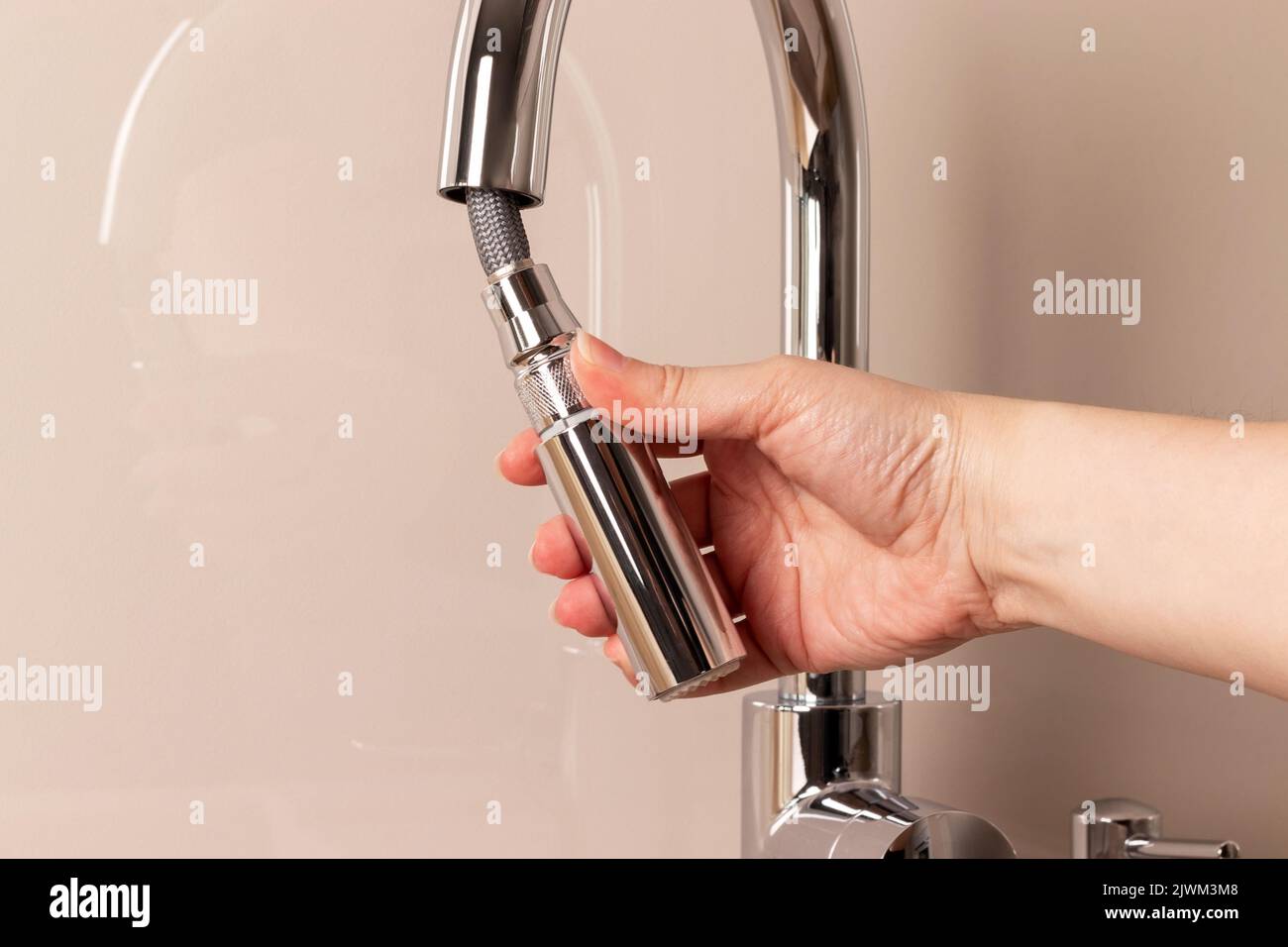 Weibliche Hand mit modernen Chrom Wasserhahn mit Remote-Schlauch. Küchenarmatur mit Ausziehauslauf Stockfoto