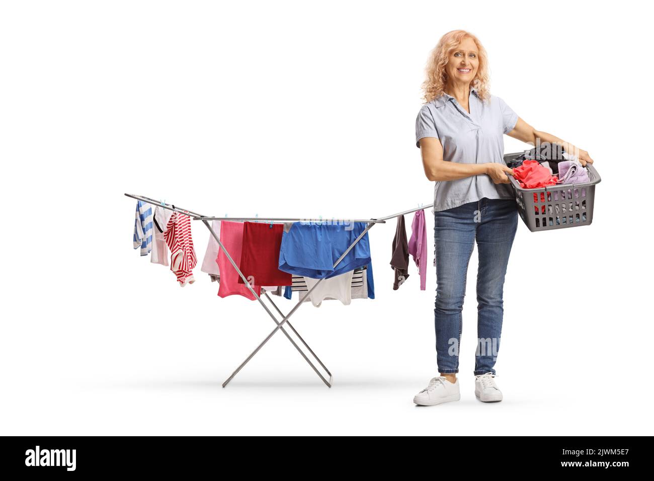 In voller Länge Porträt einer Frau mit einem Wäschekorb neben einem Wäscheständer mit isolierten Kleidungsstücken auf weißem Hintergrund Stockfoto