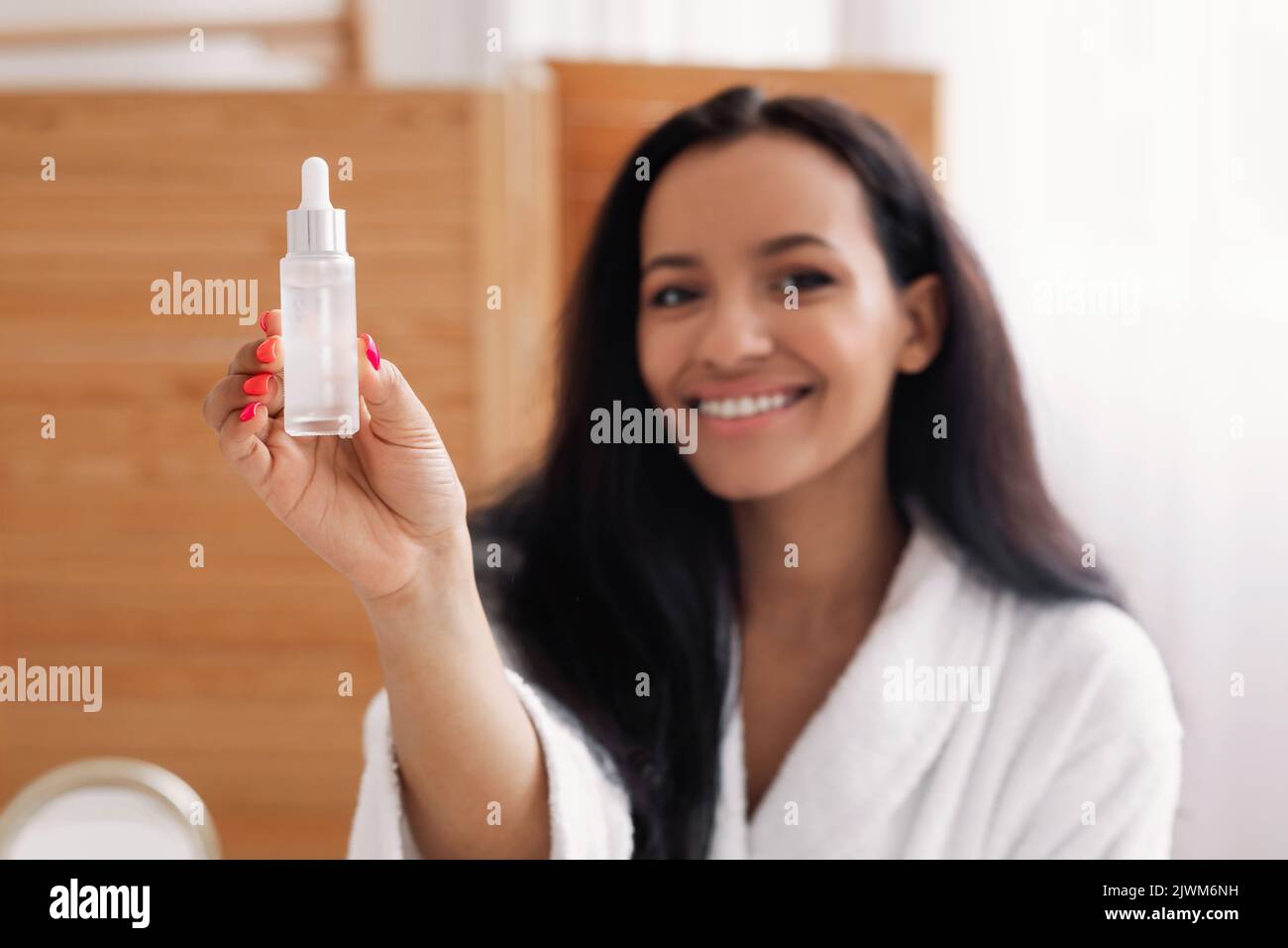 Fröhliche Schwarze Frau Zeigt Serumflasche Im Modernen Badezimmer Stockfoto