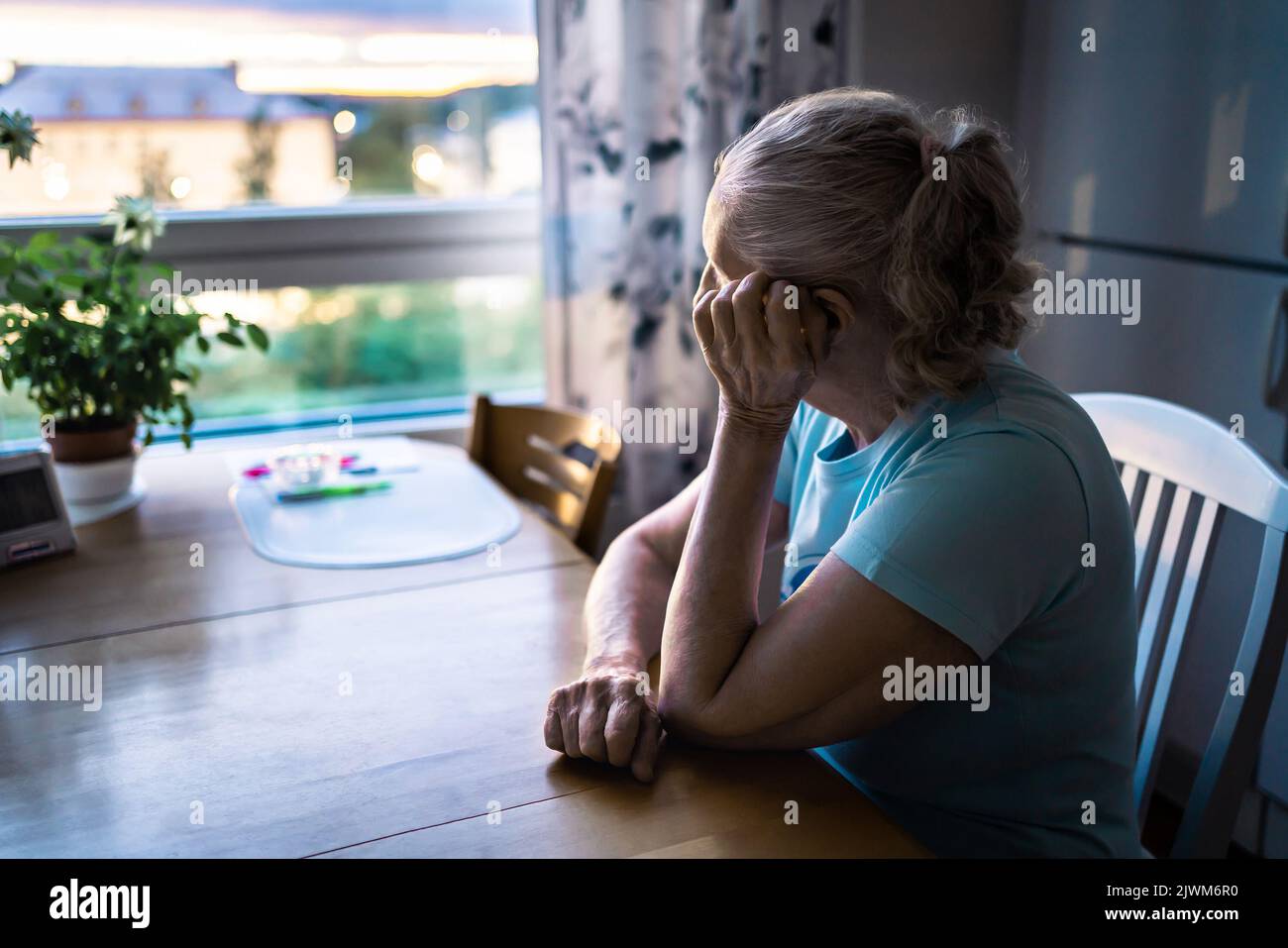 Traurige alte Frau. Depressive einsame ältere Dame mit alzheimer, Demenz, Gedächtnisverlust oder Einsamkeit. Ältere Person, die aus dem Fenster des Hauses schaut. Stockfoto