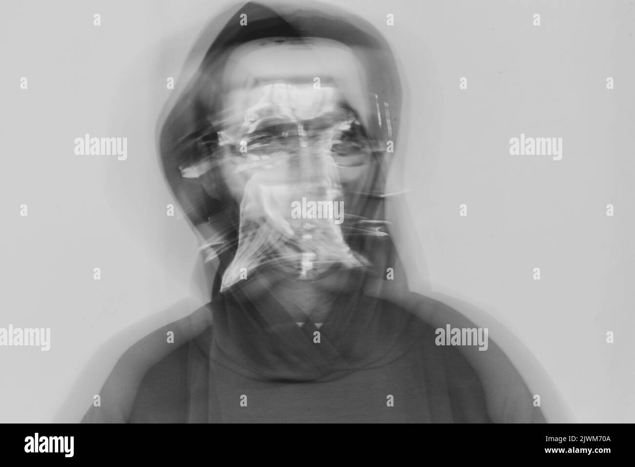 Ein Mädchen in einer Vollmaske aus Kunststoff und in einer Kapuze auf einem isolierten Hintergrund schüttelt ihren Kopf bei einer langen Exposition, Anonymität, Schreien und Verzweiflung, Psych Stockfoto