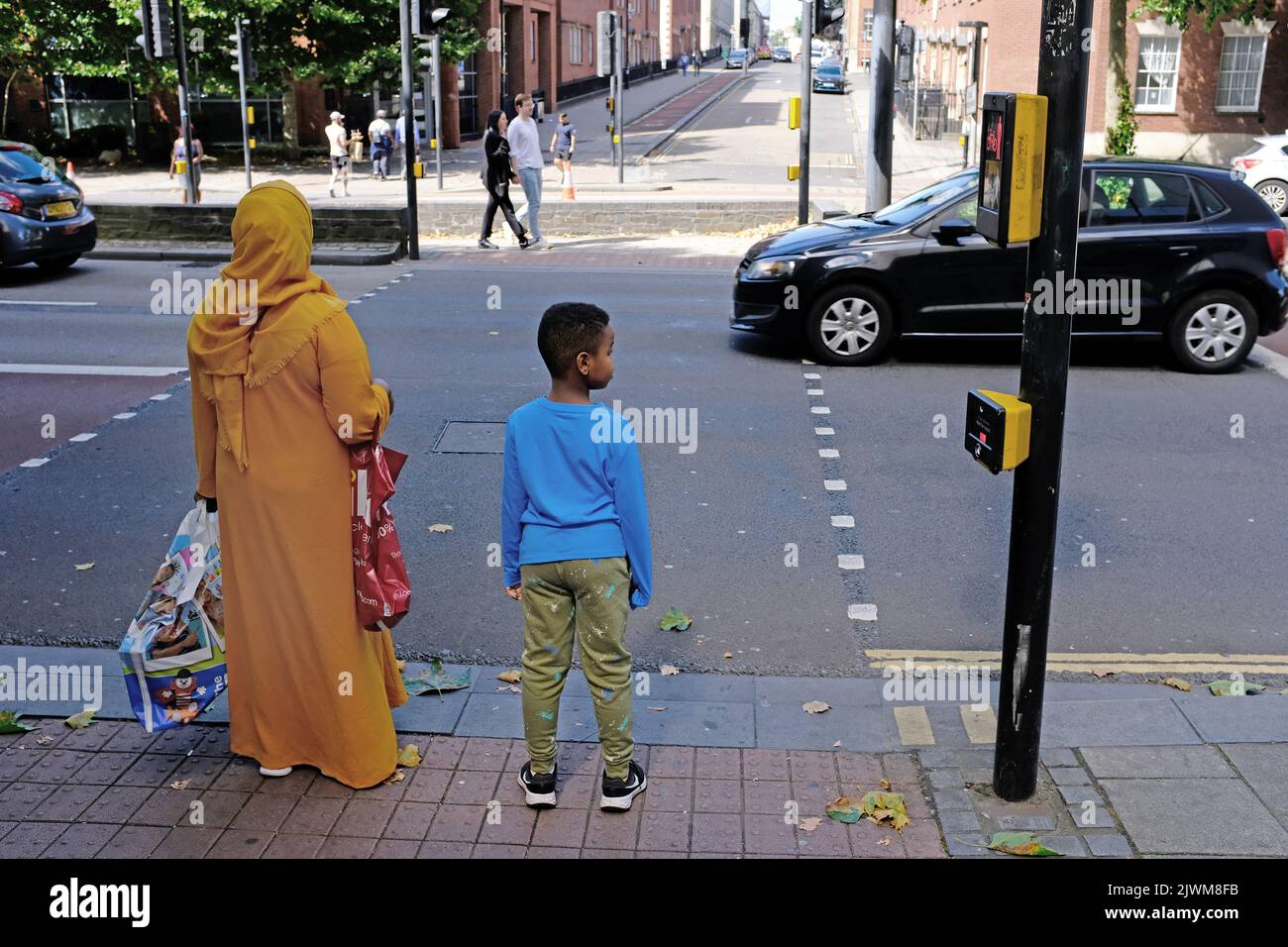 Eine muslimische Mutter und ihr Sohn warten darauf, die Straße in einer belebten Straße in Bristol zu überqueren. Stockfoto