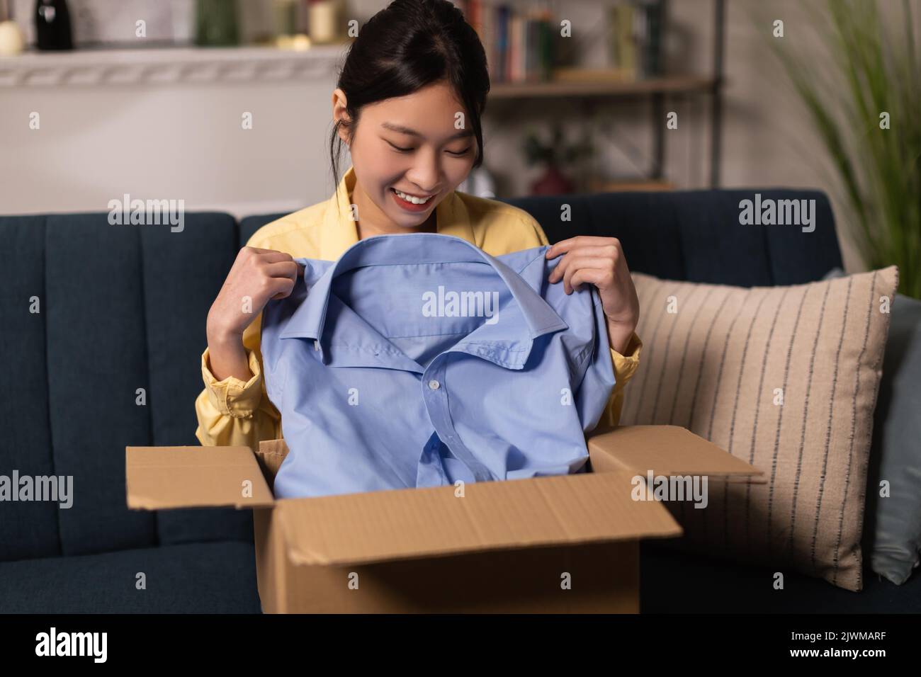 Fröhliche Chinesische Dame Auspacken Box Hält Blaues Shirt Zu Hause Stockfoto