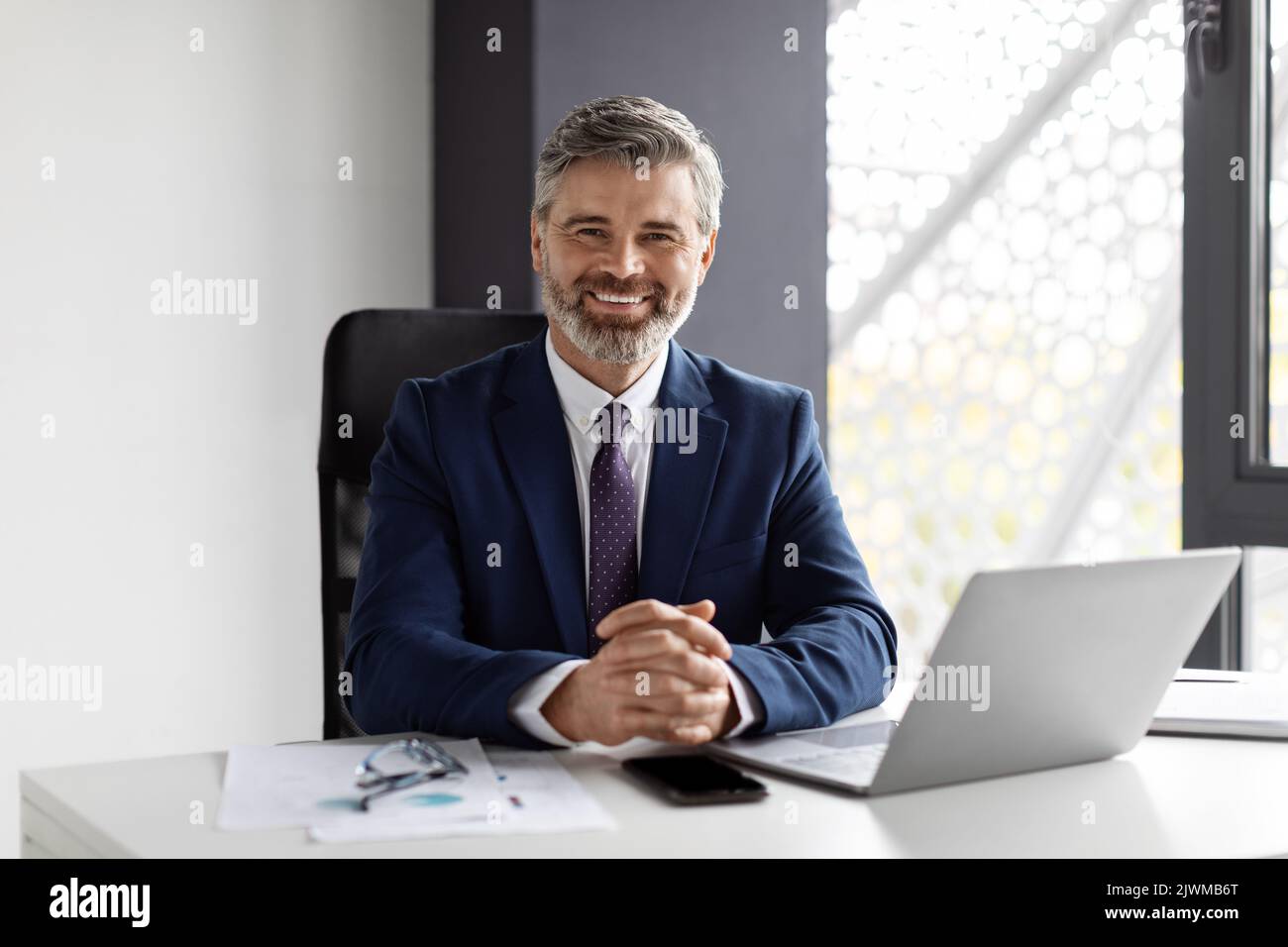 Porträt Eines Gutaussehenden Lächelnden Geschäftsmannes Mittleren Alters, Der Am Arbeitsplatz Im Büro Sitzt Stockfoto