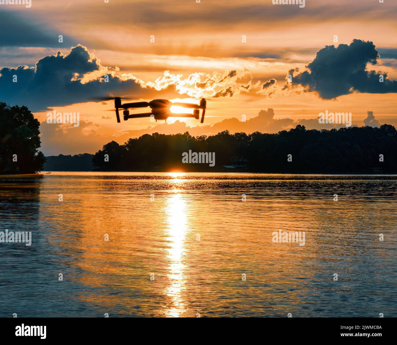 Silhouette einer Drohne, die über einen See in den Sonnenuntergang fliegt. Stockfoto