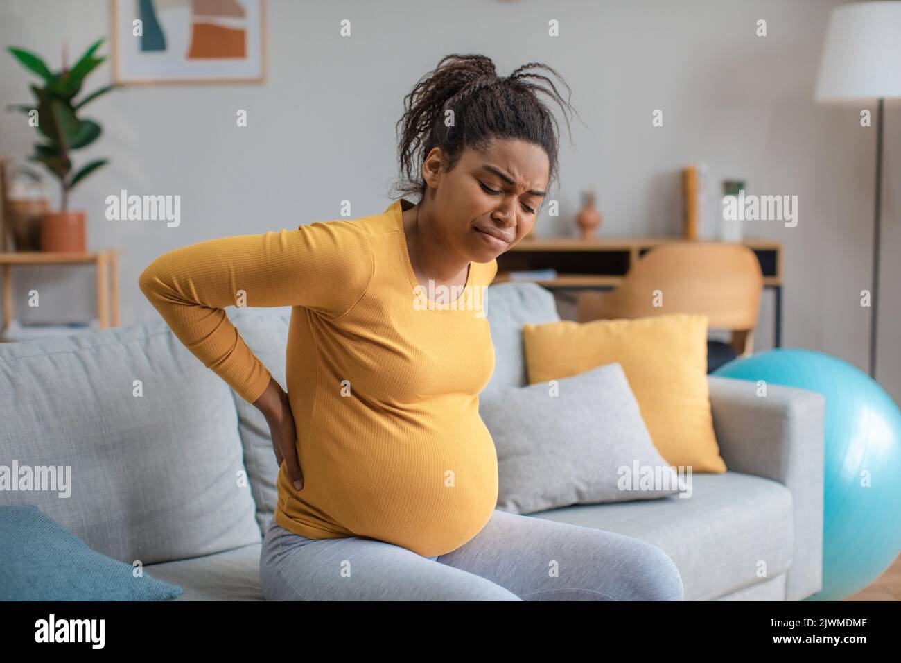 Traurige junge, schwanger afroamerikanische Dame mit großem Bauch, die unter Rückenschmerzen im Wohnzimmer leidet Stockfoto