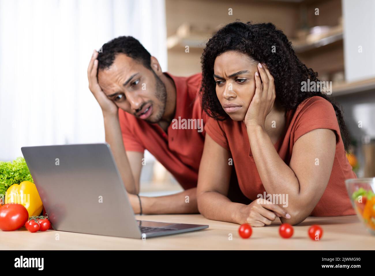 Unglücklich traurig junge afroamerikanische Paar in gleichen T-Shirts Blick auf Laptop, finden Fehler in der Küche Interieur Stockfoto