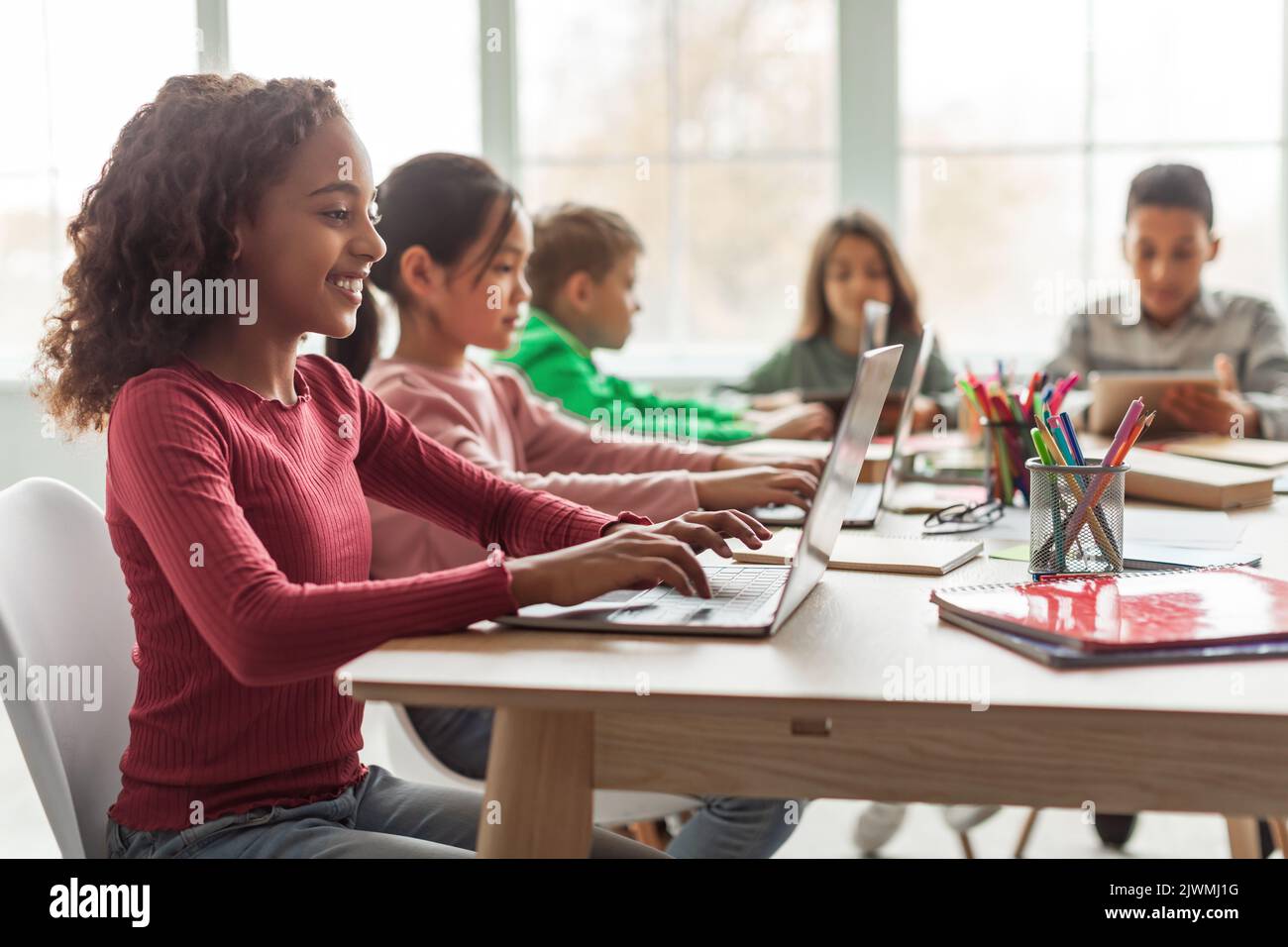Schwarz Schulmädchen Mit Laptop Sitzen Mit Multiethnischen Klassenkameraden Im Klassenzimmer Stockfoto