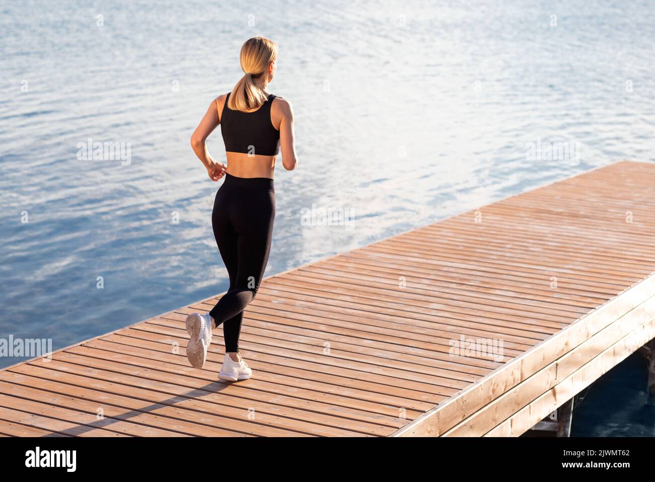 Morgenlauf. Rückansicht Des Sportlichen Blonden Weiblichen Joggens Im Freien In Der Nähe Des Flusses Stockfoto