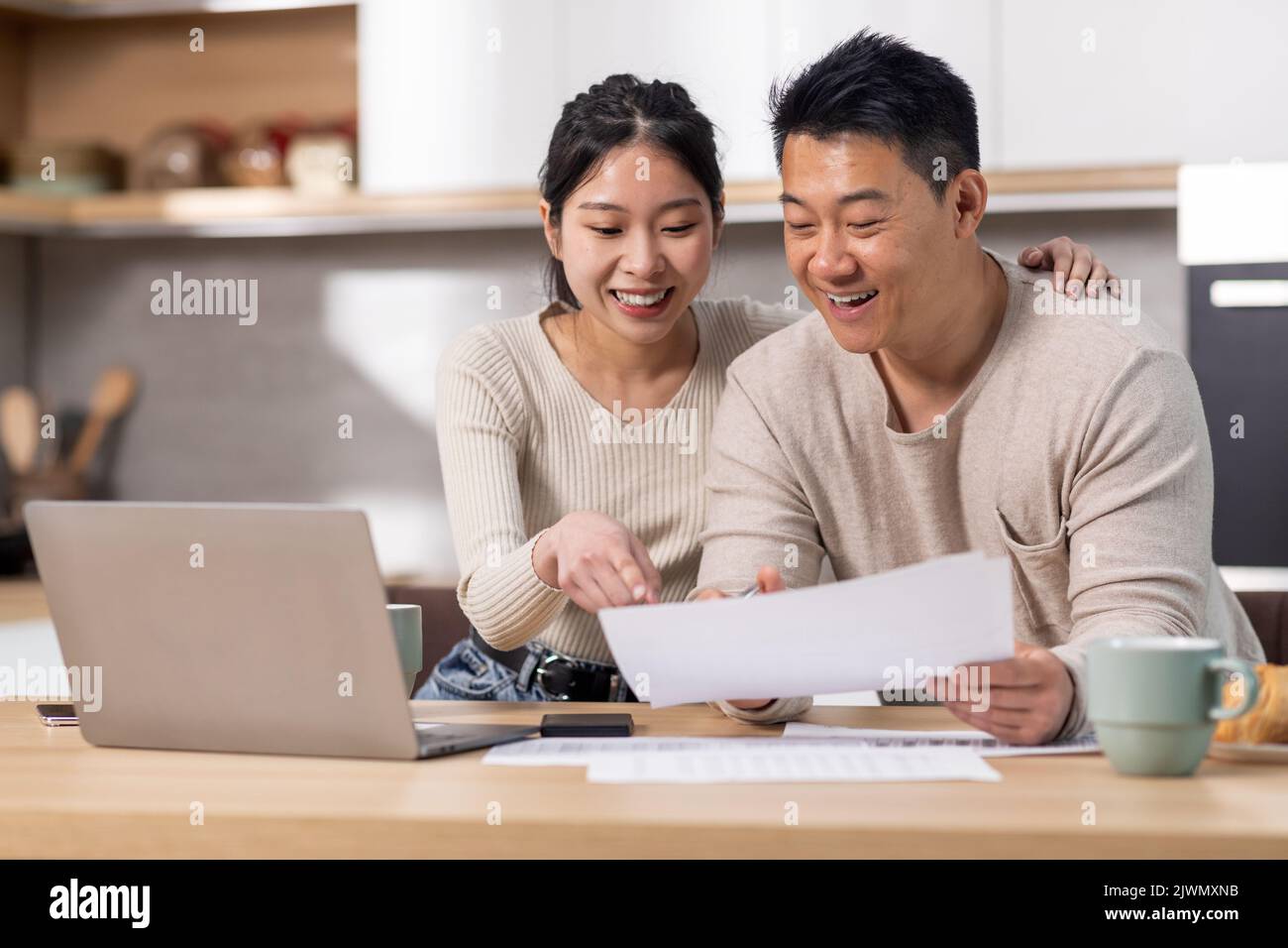 Fröhliche asiatische Ehegatten zahlen Rechnungen über das Internet, mit Laptop Stockfoto