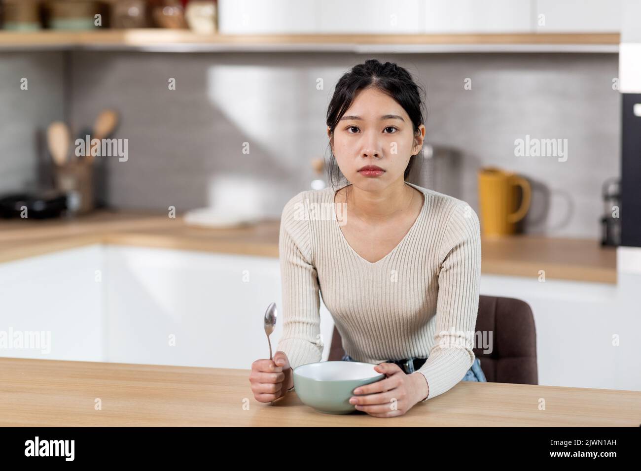 Hungernde asiatische Frau zeigt ihren leeren Teller Stockfoto