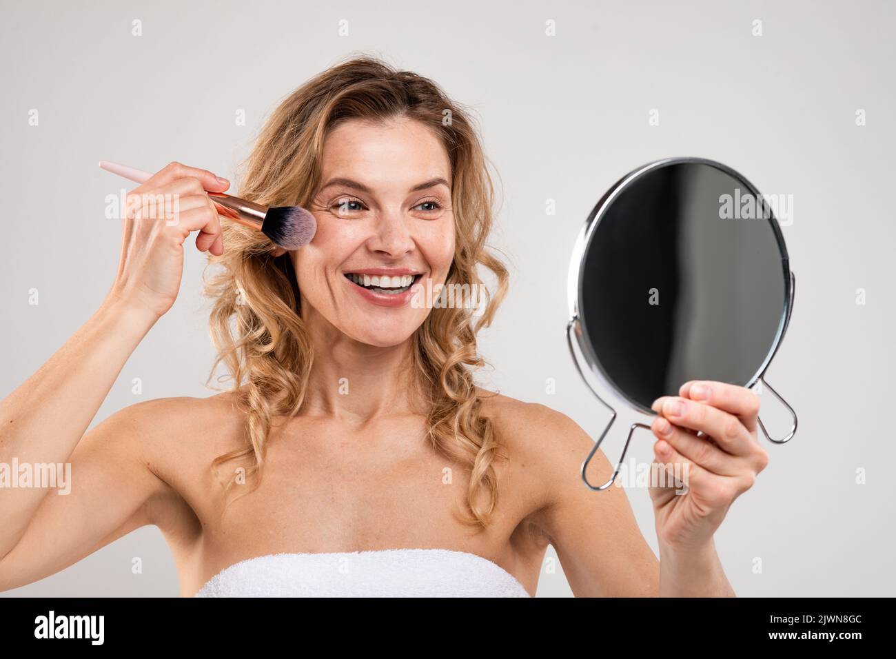 Happy Middle Aged Female Holding Mirror Und Anwendung Blush Auf Das Gesicht Stockfoto