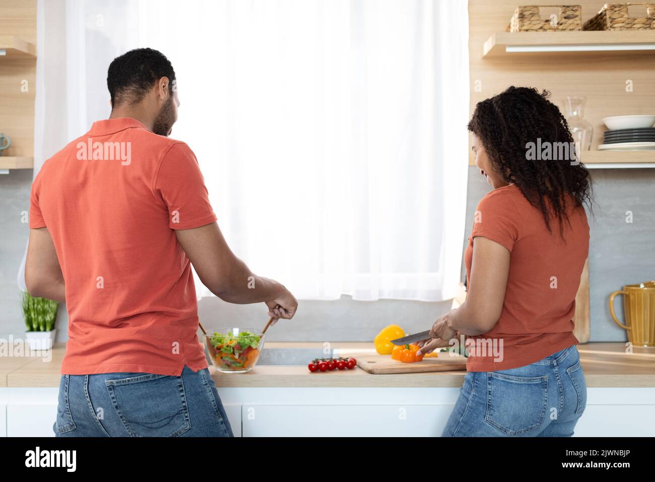 Junges afroamerikanisches Paar in gleichen T-Shirts, das zusammen mit Gemüse hausgemachtes Essen kocht Stockfoto