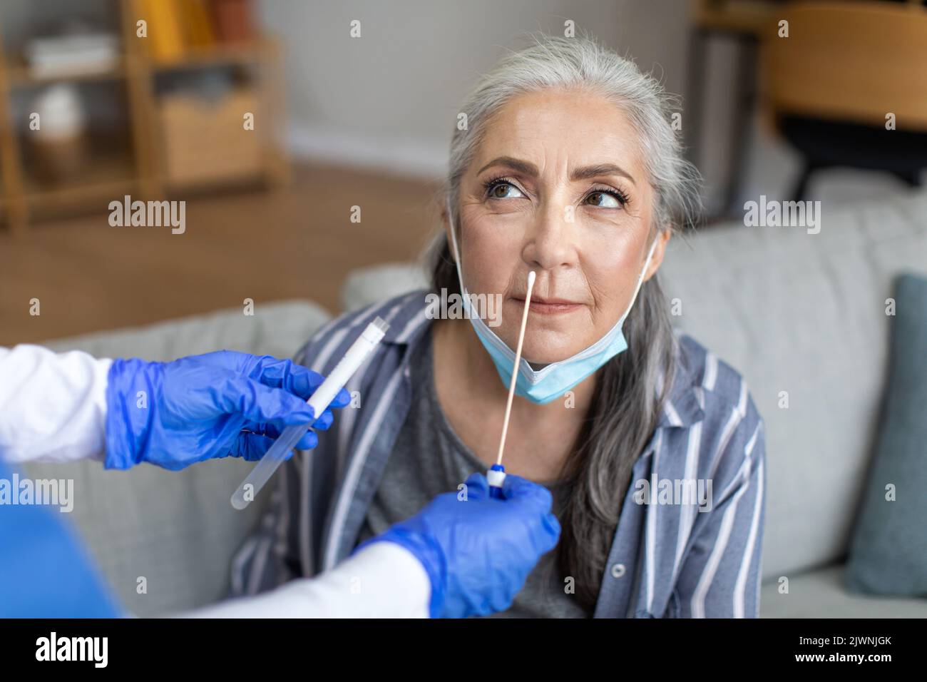 Krankenschwester in Schutzhandschuhen, die Covid-19-Test bei einer schweren kaukasischen älteren grauhaarigen Patientin im Zimmer durchführt Stockfoto