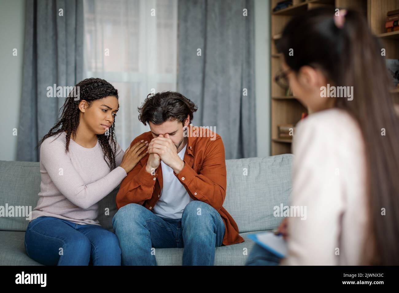 Traurige, tausendjährige schwarze Dame beruhigt den europäischen Mann bei der Begegnung mit dem Psychologen im Inneren der Büroklinik, im Kopierraum Stockfoto
