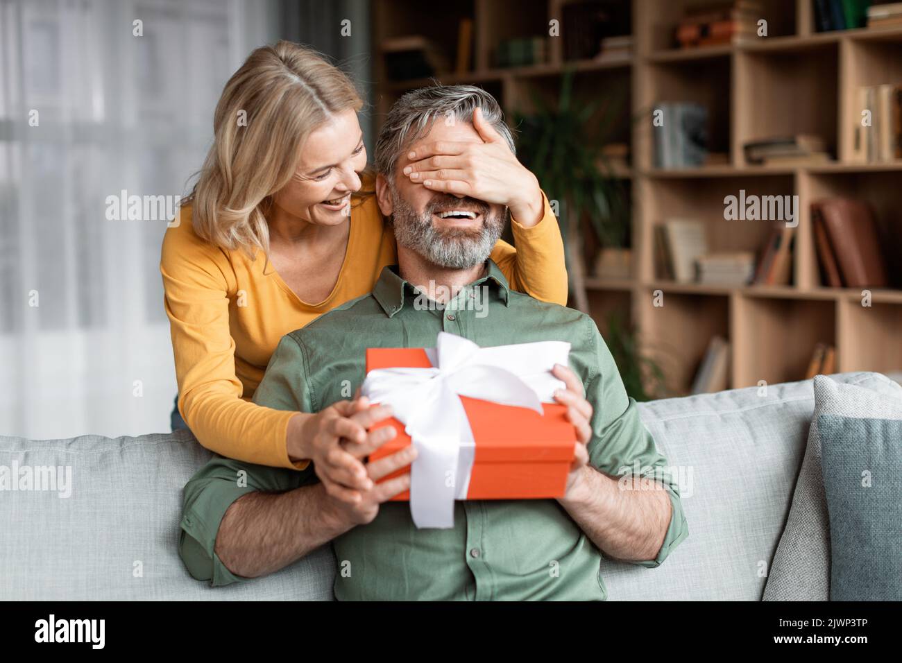 Liebevolle Frau Überraschende Mann Im Mittleren Alter Mit Geschenk Zu Hause Stockfoto