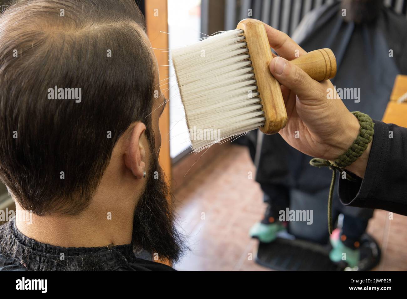 Interieur eines Friseurshopfes mit einem Kunden mit kurzen Haaren und einem sitzenden Bart, Service, während ein Stylist einen Pinsel hält, Werkzeuge für die persönliche Pflege Stockfoto
