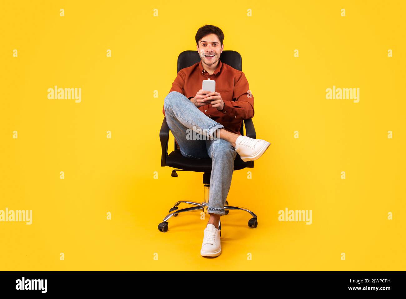 Glücklicher Mann Mit Mobiltelefon Sitzt Im Bürostuhl, Gelber Hintergrund Stockfoto