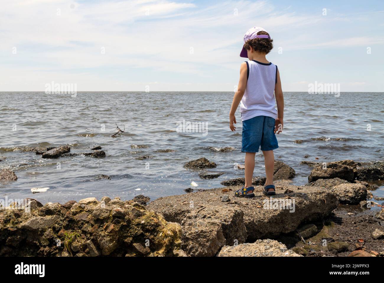 Kleiner Junge, der vom Ufer aus auf verschmutzten Fluss schaut, Umweltkonzept Stockfoto