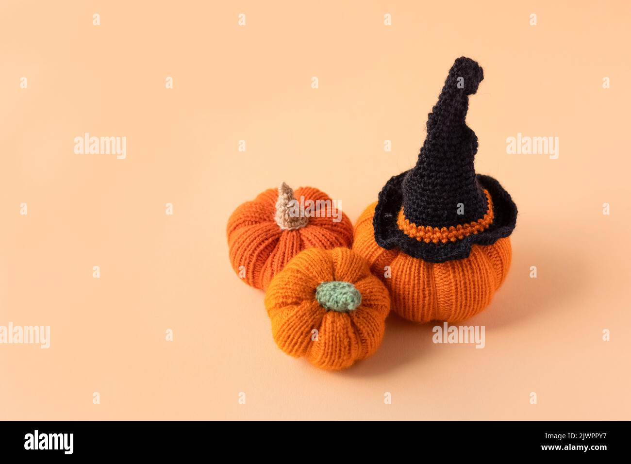 Gestrickte orangefarbene Kürbisse mit schwarzem Hexenhut auf orangefarbenem Hintergrund, Herbstkomposition, Vorderansicht. Halloween-Konzept. Stockfoto