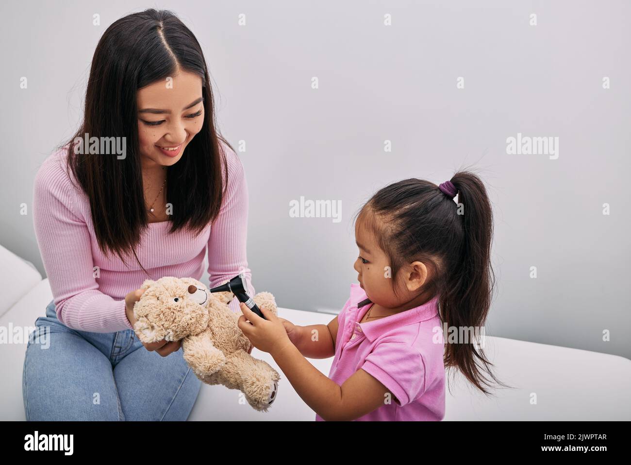 Asiatische Mädchen spielt mit ihrem Spielzeug Bär in medizinischen Spiel, mit Otoskop mit Unterstützung ihrer Mutter. Hörklinik für Kinder Stockfoto