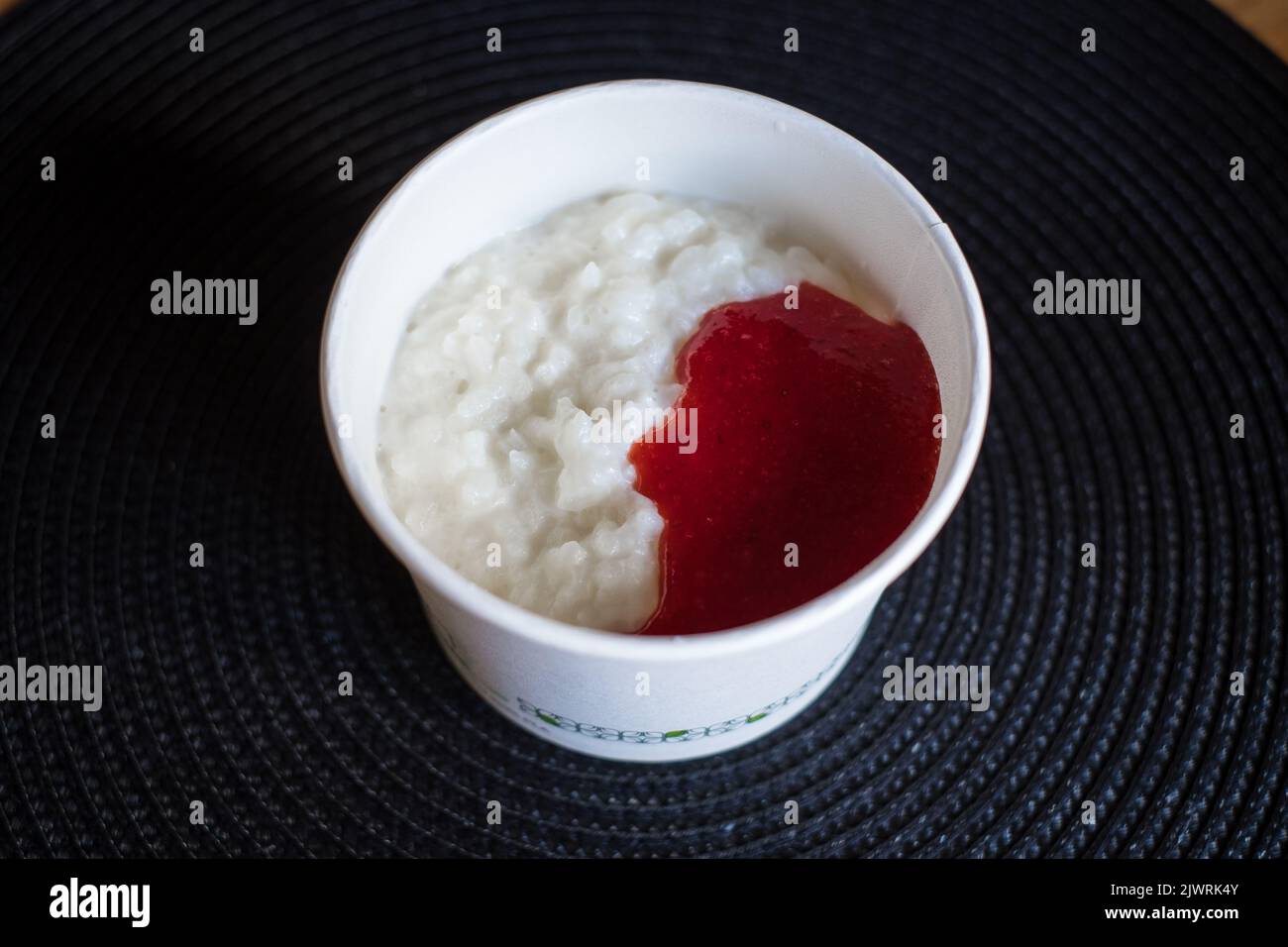 Reisflockenporridge in einem weißen runden Karton mit frischer Erdbeermarmelade zum Mitnehmen. Stockfoto
