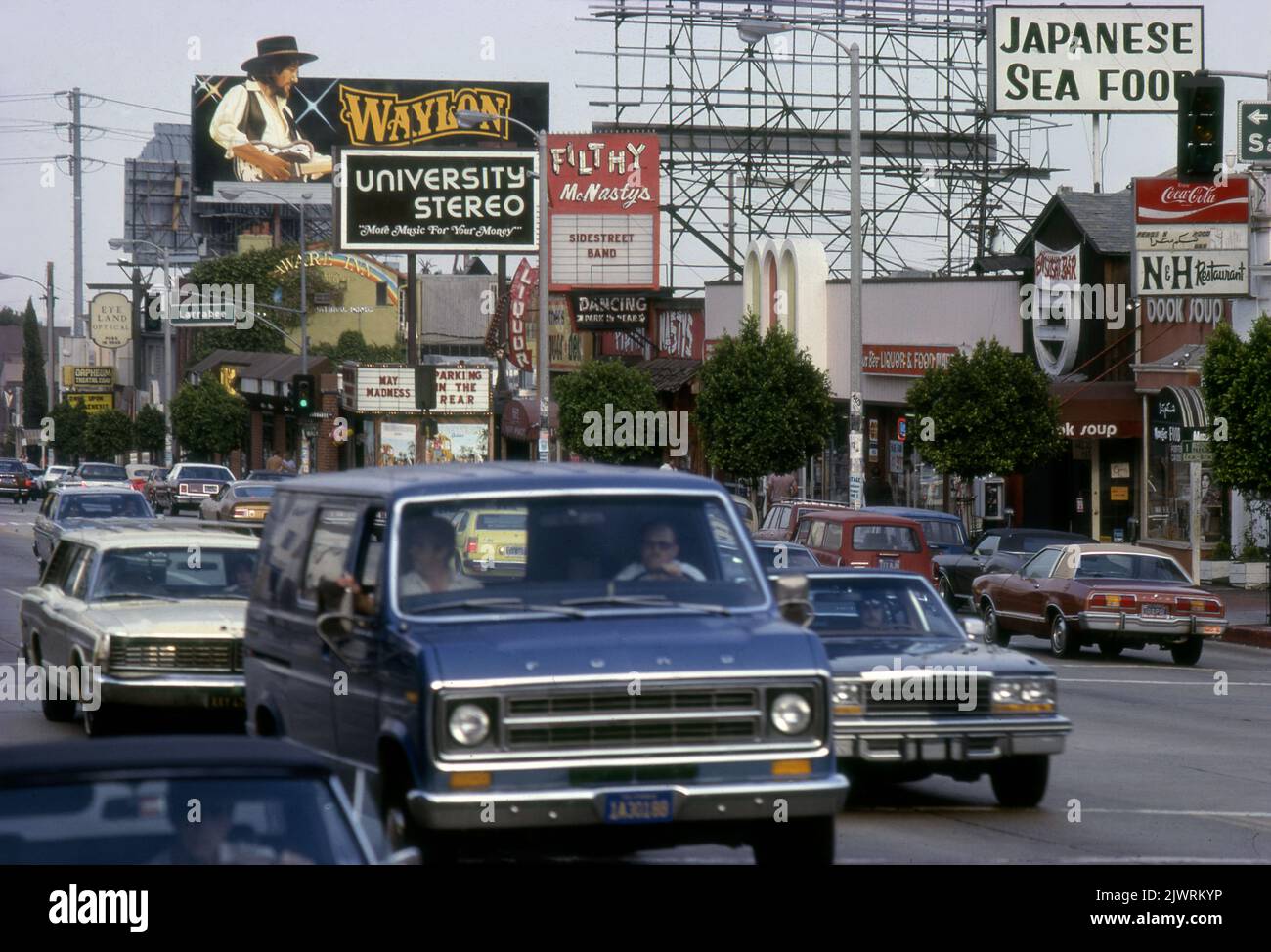Der Sunset Strip um 1970s mit Verkehr, Waylon Jennings Plakatwand und marquis für den Nachtclub Filthy Mc Nasty in Los Angeles, CA Stockfoto