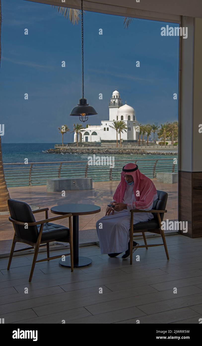 Arabischer Mann im Café mit Inselmoschee im Hintergrund Jeddah Corniche Saudi-Arabien Stockfoto