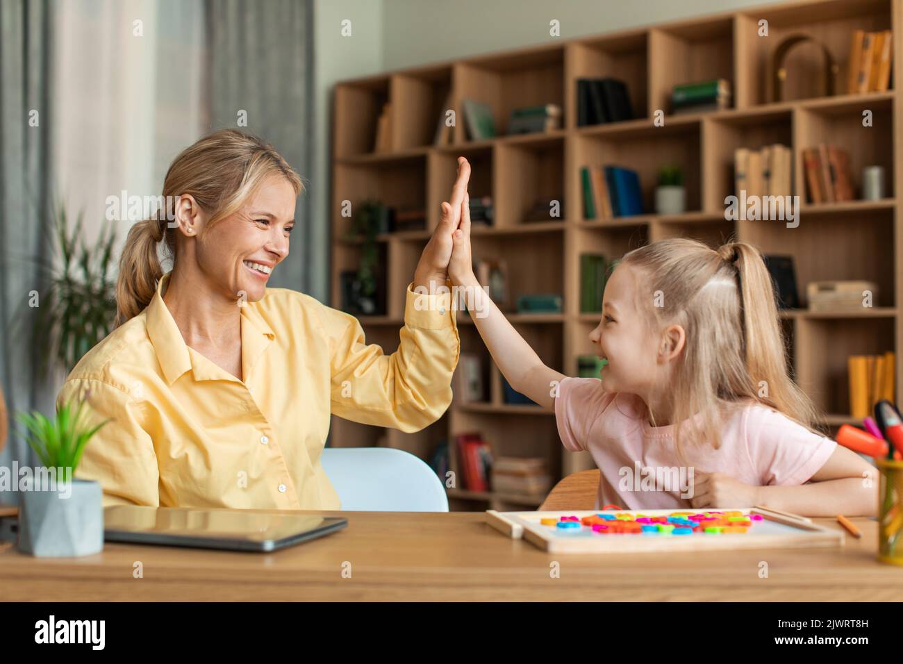 Glückliches hübsches Mädchen, das ihrem Lehrer fünf hohe, Frau und Kind Vorschulkinder beim Lernen von Alphabet während des Privatunterrichts gibt Stockfoto