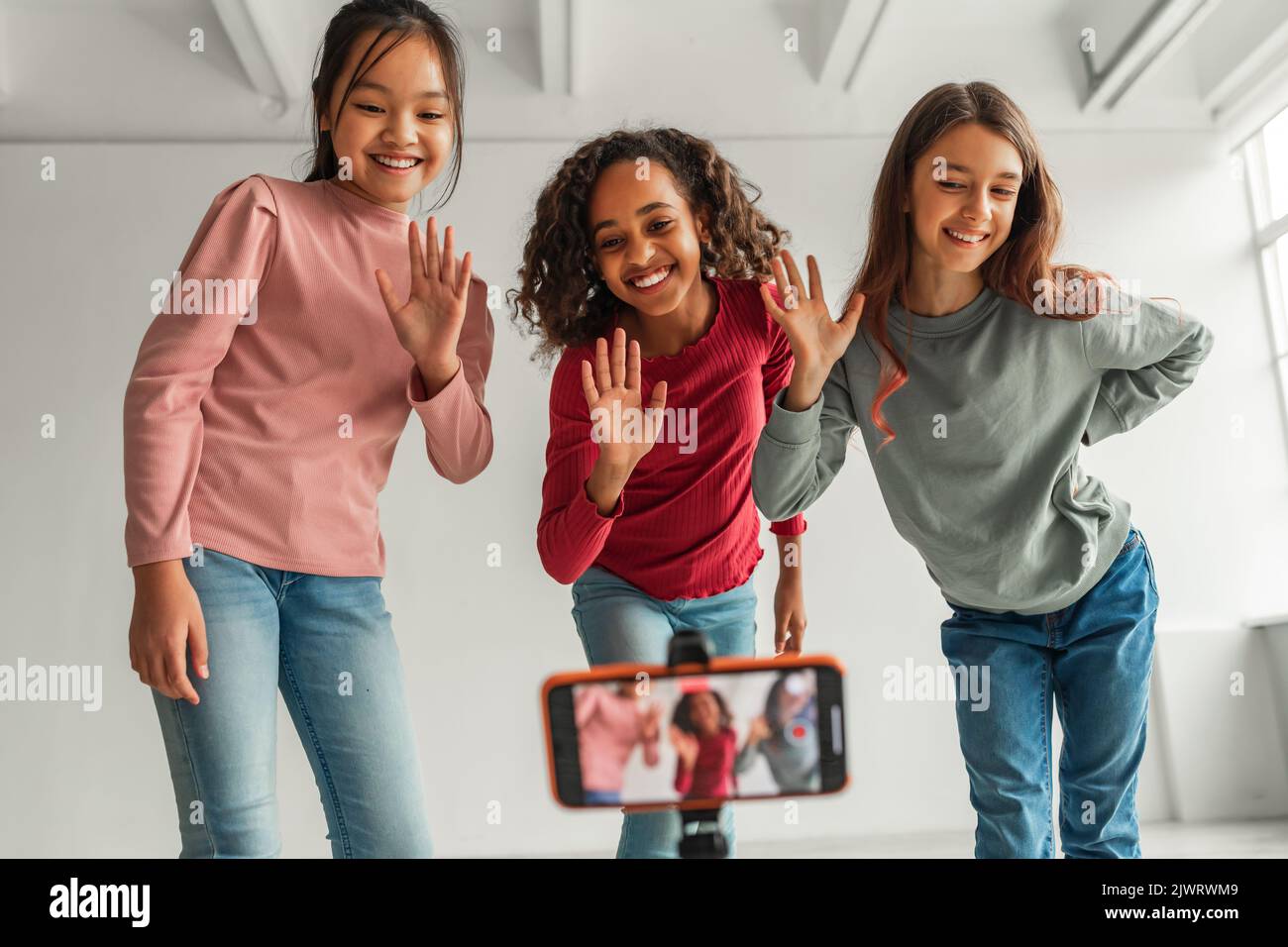 Drei Glückliche Verschiedene Mädchen Winken Hände Auf Smartphone Im Innen Stockfoto