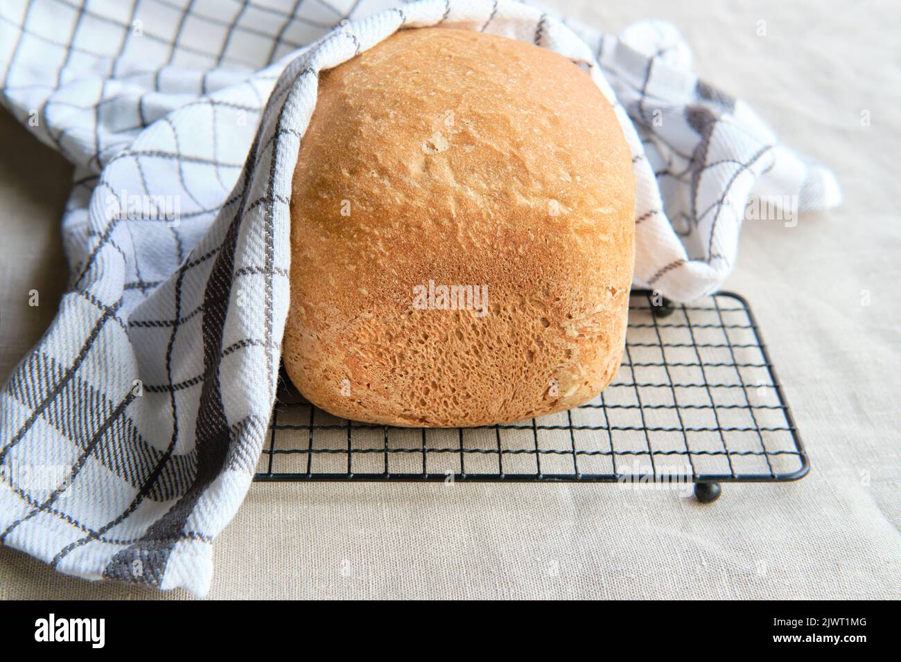 Hausgemachtes Bauernhaus gemischtes Brot. Nahaufnahme von Brot, das in der Backmaschine gebacken wurde. Vollkornbrot auf Trockengestell mit gestreifem Handtuch auf Textil Stockfoto