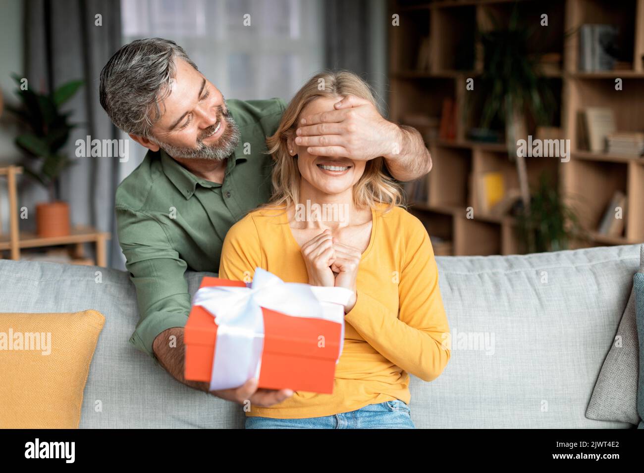 Angenehme Überraschung. Liebevoller Mann mittleren Alters, der die Augen der Frau bedeckt und Geschenke macht Stockfoto