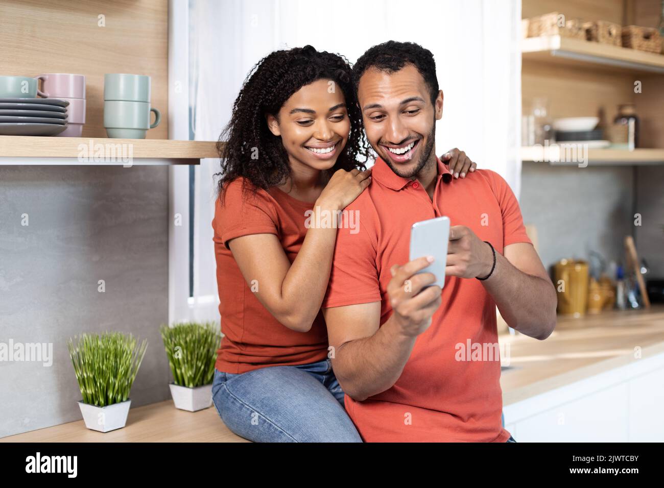 Lächelnde junge afroamerikanische Männer und Frauen in gleichen T-Shirts führen einen Videoanruf auf dem Smartphone oder schauen sich ein Video an Stockfoto