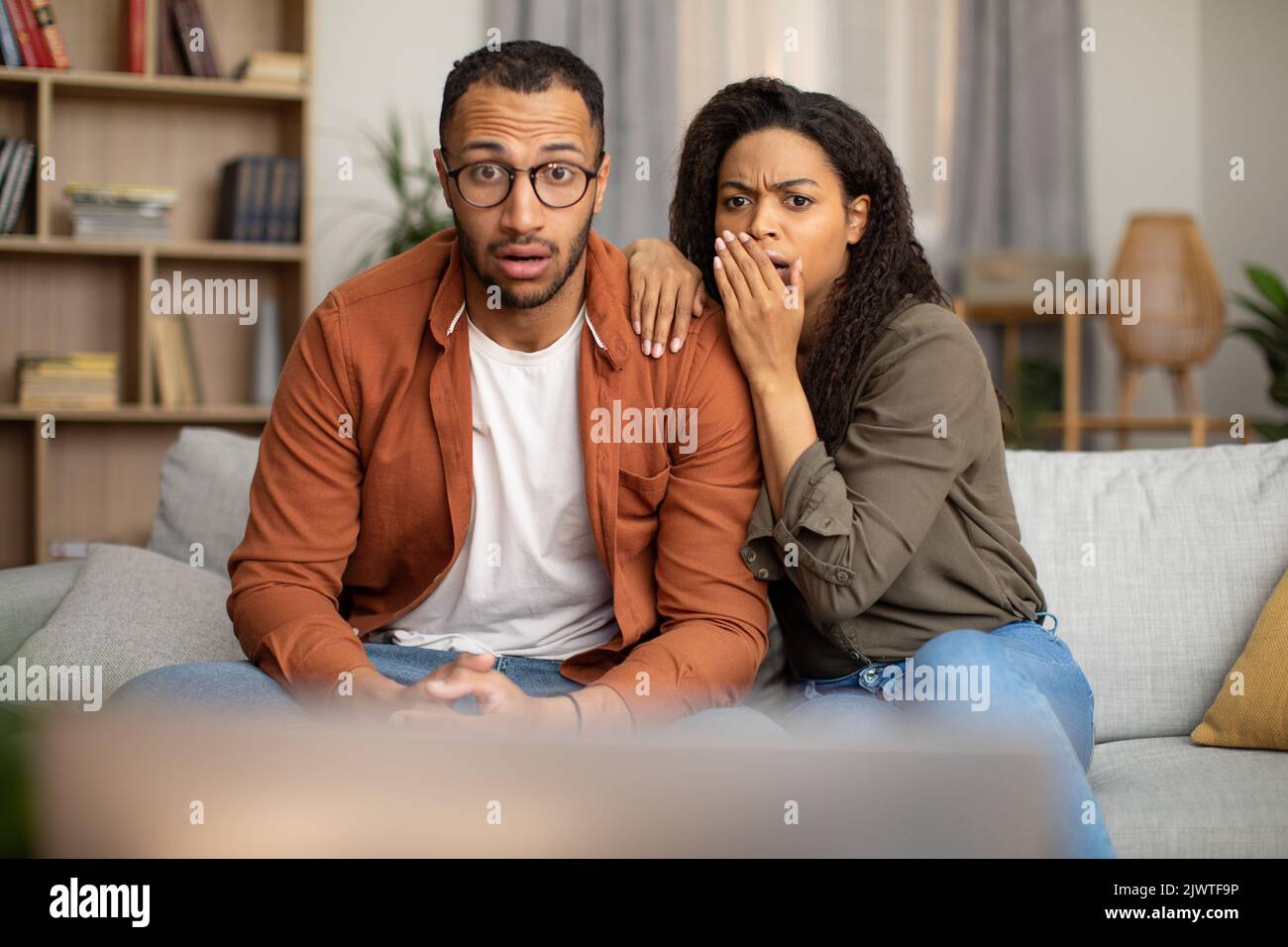 Schockiert afroamerikanisches Paar, das zu Hause schockierende TV-Inhalte ansieht Stockfoto