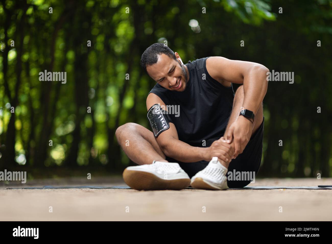 afroamerikanischer Athlet, der Schmerzen hat und seinen Knöchel berührt Stockfoto