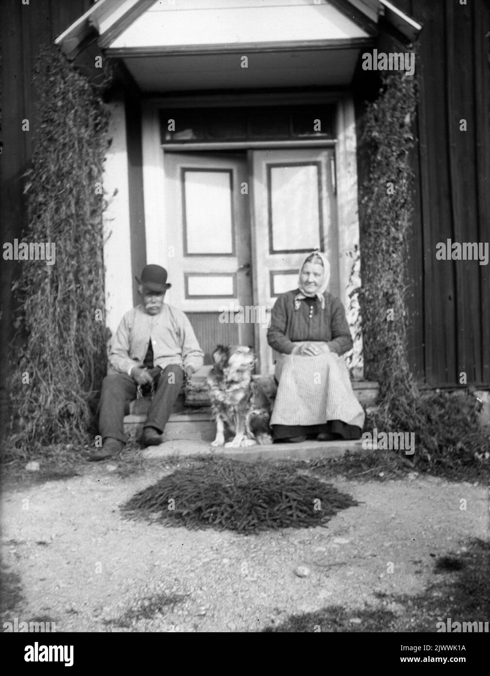 Åsmundshyttan Nr. 7, Isaksberg. Auf der Treppe befindet sich Brita Stina Pehrsdotter, geboren am 4. September 1858, gestorben am 6. Februar 1940. Und ihr Mann Johan Wretling, geboren am 12. Oktober 1856, starb am 11. Dezember 1940. Das Bild ist in Torsåkers photo -historical company enthalten. Abbildung 7: 2. Åsmundshyttan Nr 7, Isaksberg. på trappan sitter Brita Stina Pehrsdotter född 4. september 1858, död 6 februari 1940. Och hennes Make Johan Wretling född 12 oktober 1856, död 11 dezember 1940. Bilder finns med i Torsåkers Fotohistoriska Sällskap. Bild 7:2. Stockfoto