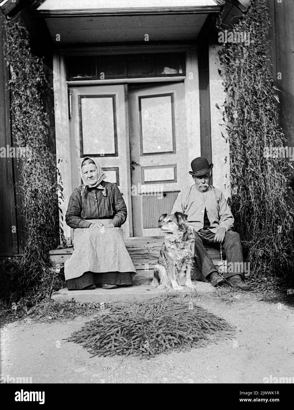 Åsmundshyttan Nr. 7, Isaksberg. Auf der Treppe befindet sich Brita Stina Pehrsdotter, geboren am 4. September 1858, gestorben am 6. Februar 1940. Und ihr Mann Johan Wretling, geboren am 12. Oktober 1856, starb am 11. Dezember 1940. Das Bild ist in Torsåkers photo -historical company enthalten. Abbildung 7: 2. Åsmundshyttan Nr 7, Isaksberg. på trappan sitter Brita Stina Pehrsdotter född 4. september 1858, död 6 februari 1940. Och hennes Make Johan Wretling född 12 oktober 1856, död 11 dezember 1940. Bilder finns med i Torsåkers Fotohistoriska Sällskap. Bild 7:2. Stockfoto