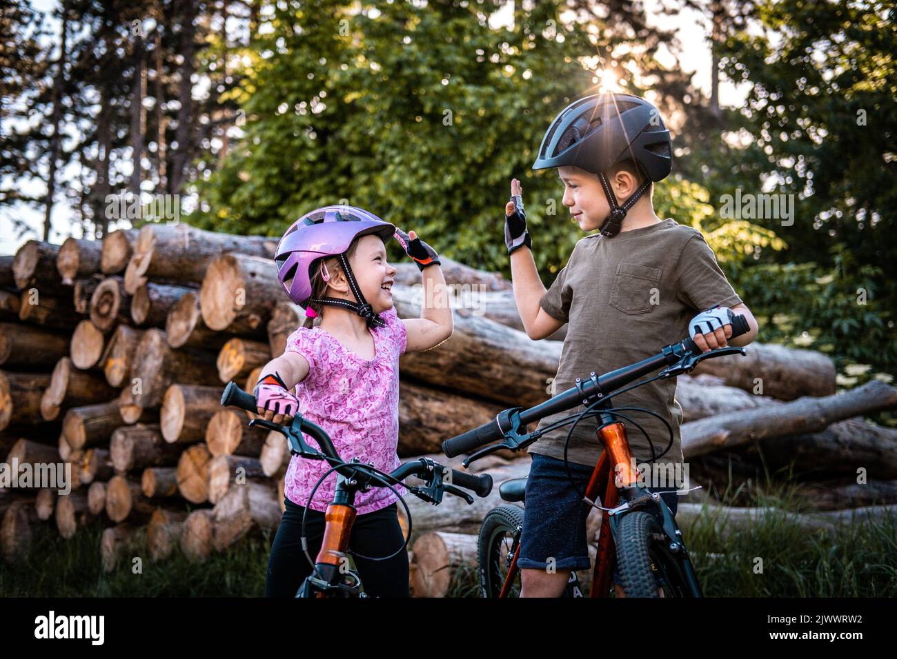 Zwei glückliche Kinder mit Fahrradhelmen geben beim Radfahren im Wald hohe fünf Stockfoto