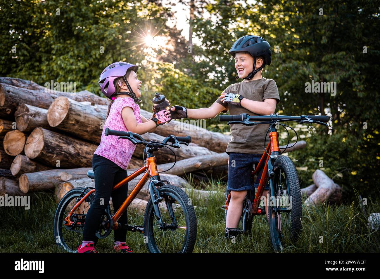 Zwei lächelnde Kinder mit Fahrradhelmen passieren beim Radfahren die Flasche Stockfoto