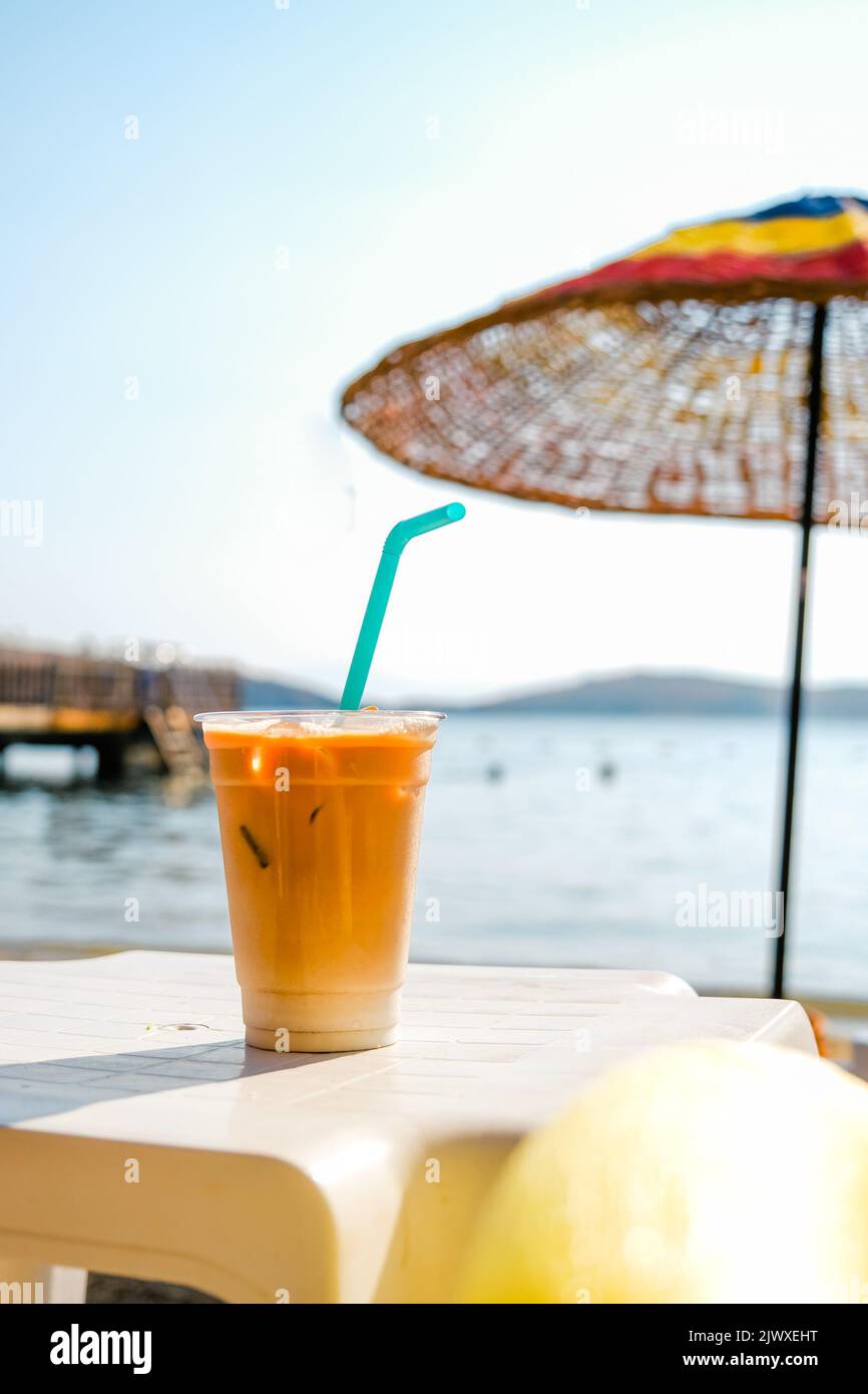 Eis-Latte-Kaffee in Plastikglas am Strand. Stockfoto