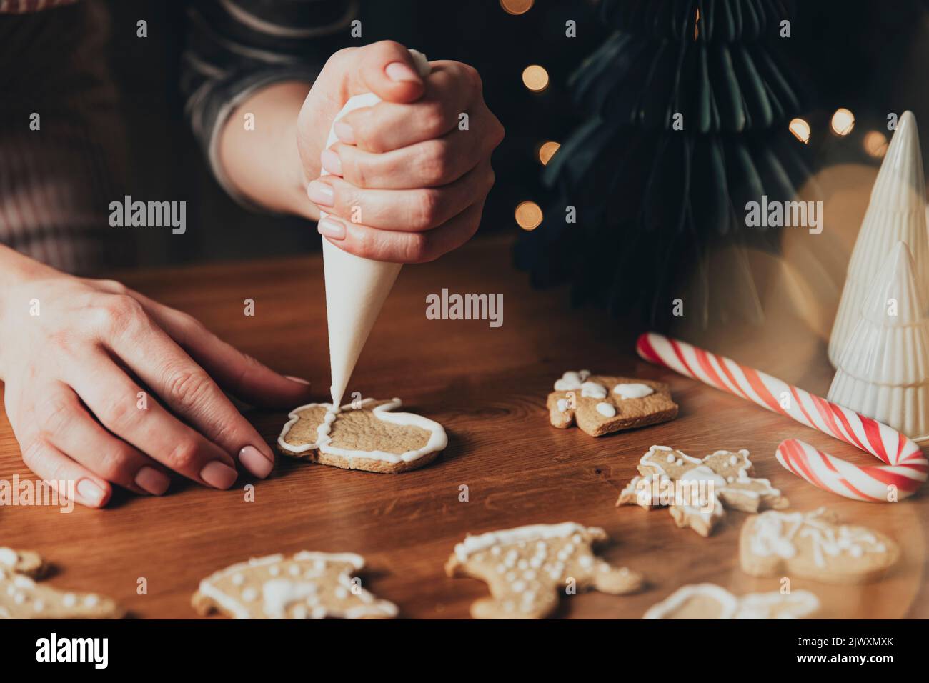 Weihnachten, Neujahr Lebensmittelzubereitung. Xmas Lebkuchen Kochen, Herstellung und Dekoration frisch gebackene Kekse. Nahaufnahme eines abgeschnittenen Schusses mit weiblichen Händen, die das Sahnehäubchen und den Mastix halten und Kekse dekorieren Stockfoto