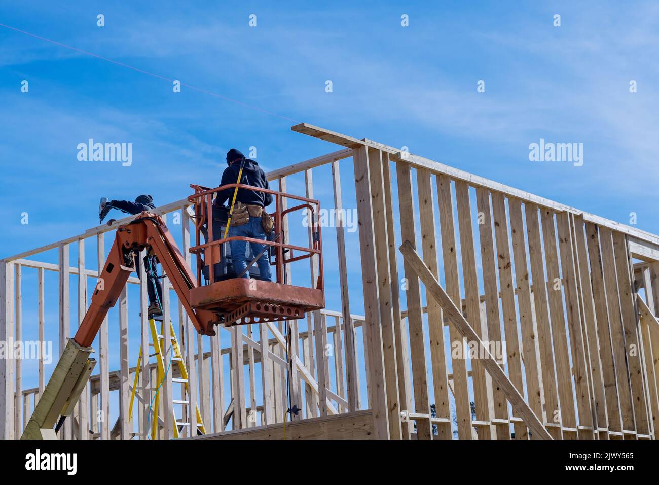 Mit einem Lufthammer ein Haus bauen, in dem ein Arbeiter mit einem Lufthammer Holzrahmenbalken an das Haus annagelt Stockfoto
