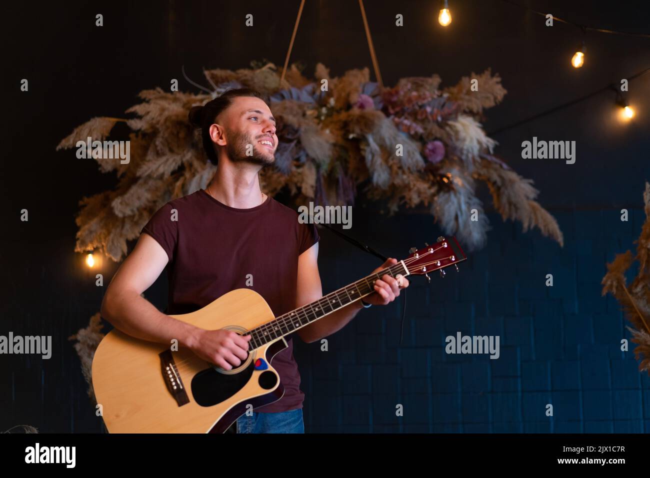 Männlicher Musiker, der akustische Gitarre spielt. Gitarrist spielt klassische Gitarre auf der Bühne im Konzert hübsch junge Hipster männlichen Gitarrist führen private Party stilvolle lange Haare Medium shoot Stockfoto